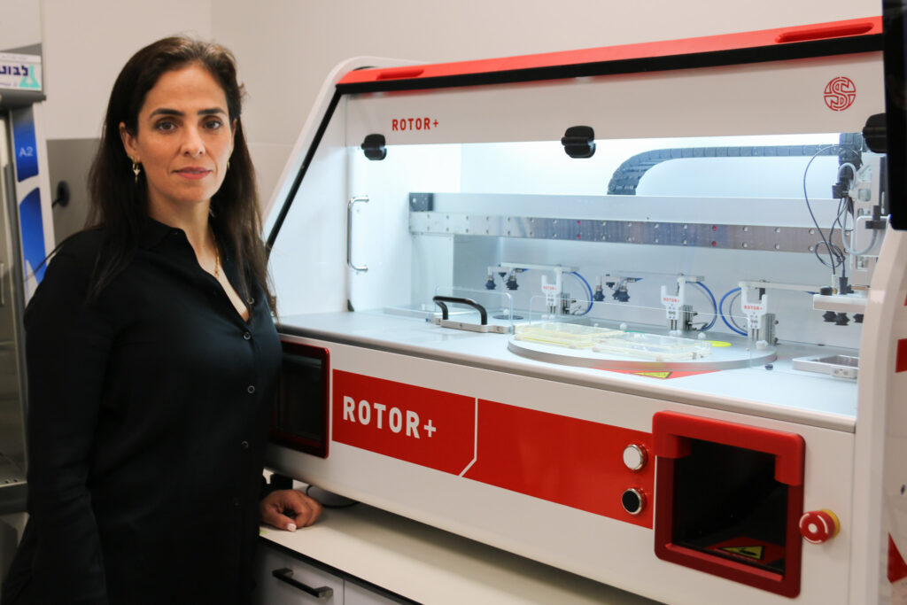 Dr Michal Breker Dekel stood by the ROTOR+, the research automation robot she uses for high throughput screening of chlamydomonas