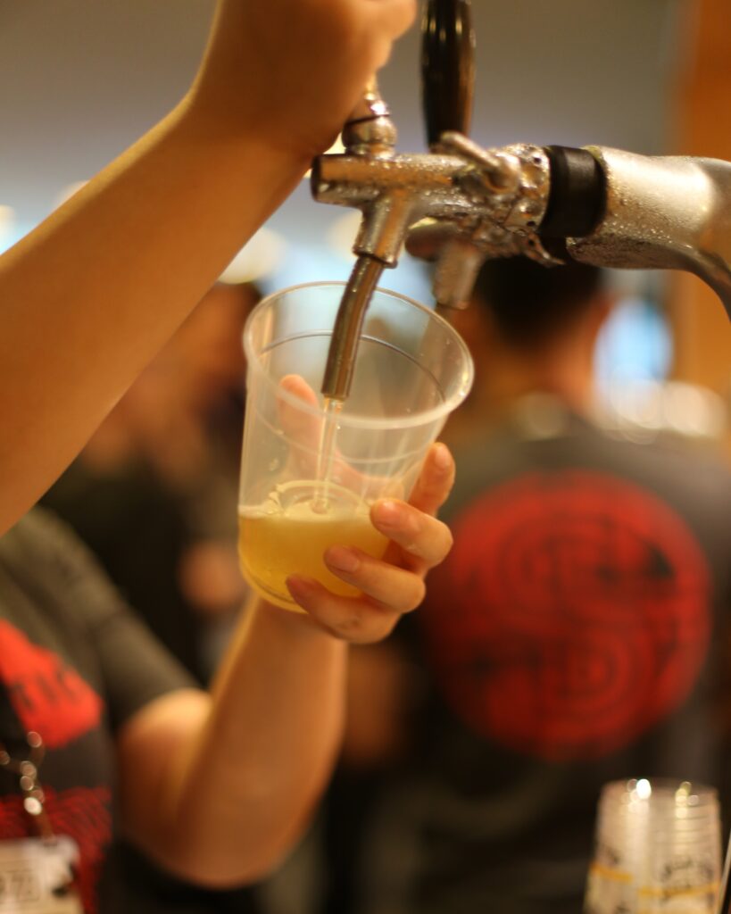 Image of a Singer Instruments employee pouring a beer into a plastic pint cup from a draft.